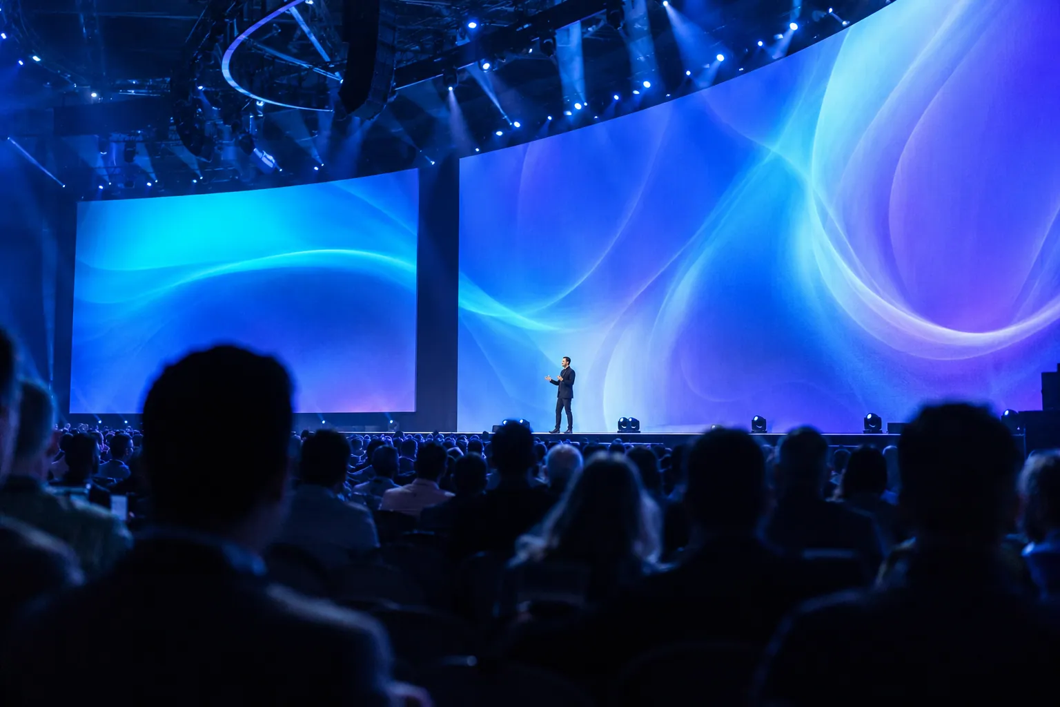 A keynote speaker on stage in front of a curved screen and a full audience